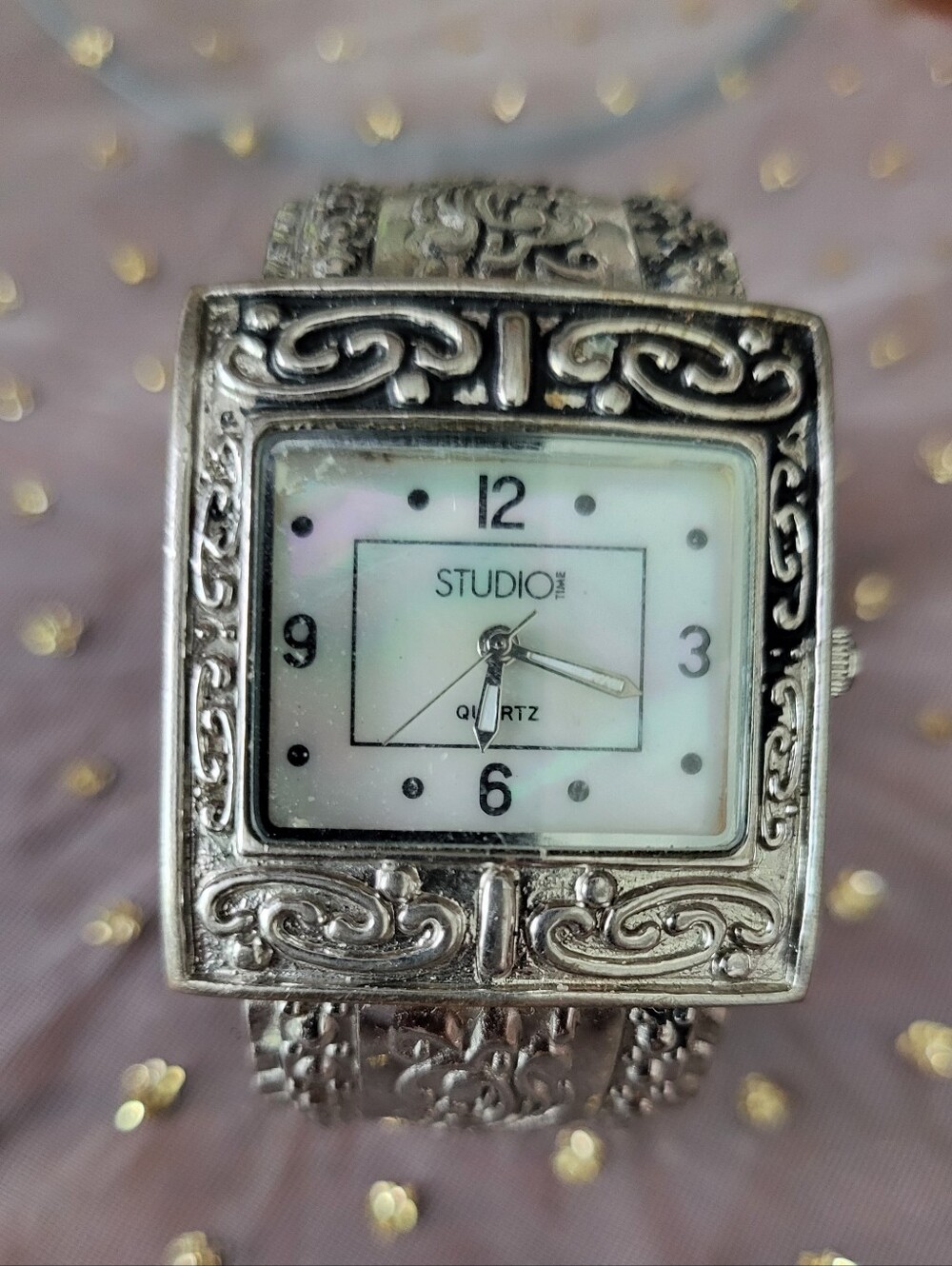 Silver bracelet watch with ornate scrollwork design has antique white face